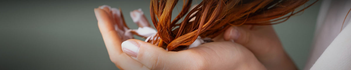 Hands working conditioner cream through the lengths of wet copper hair