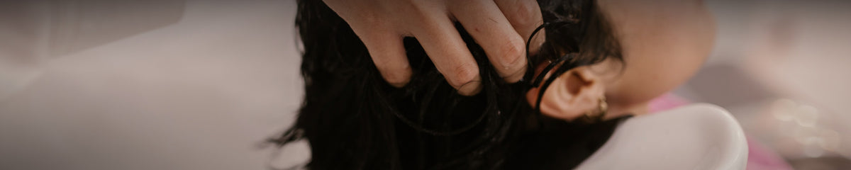 Stylist's hands shampooing a client's dark hair at a salon basin